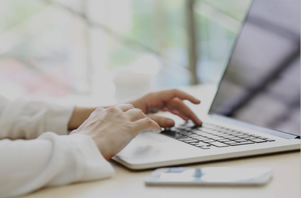 Hands typing on a laptop at a bright workspace, used for medical training or online communication.